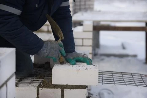 A bricklayer in mittens puts bricks in cement, close-up. Stock Photos