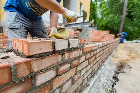 Bricklayer is near brickwork on exterior wall with putty knife in construction Stock Photos
