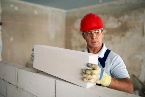 Bricklayer or mason lays bricks to construct wall of autoclaved aerated concrete Stock Photos