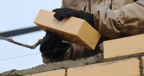 Bricklayer puts brick in cement mortar with spatula, man puts stone in wall. Stock Footage 128939276