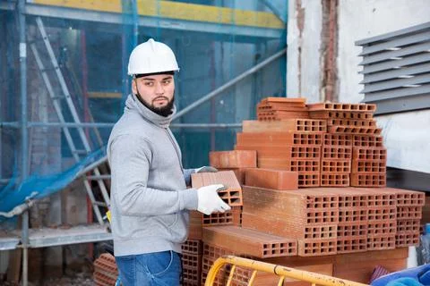 Bricklayer taking red bricks from stack Foto stock