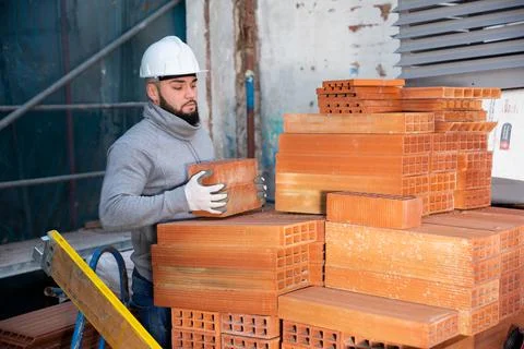 Bricklayer taking red bricks from stack Foto stock