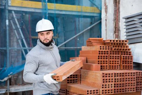 Bricklayer taking red bricks from stack Foto stock