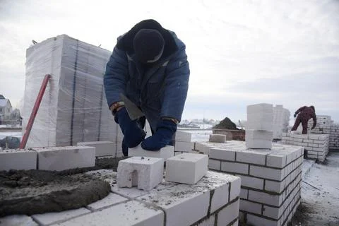 A bricklayer in winter on a construction site aligns bricks in cement. Stock Photos
