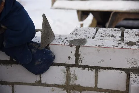 A bricklayer in winter on a construction site aligns bricks laid in cement. Stock Photos