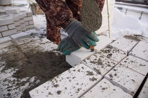 A bricklayer in winter on a construction site aligns bricks laid in cement . Stock Photos