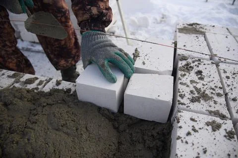 A bricklayer in winter on a construction site aligns bricks laid in cement . Stock Photos