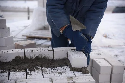 A bricklayer in winter on a construction site aligns bricks laid in cement . Stock Photos