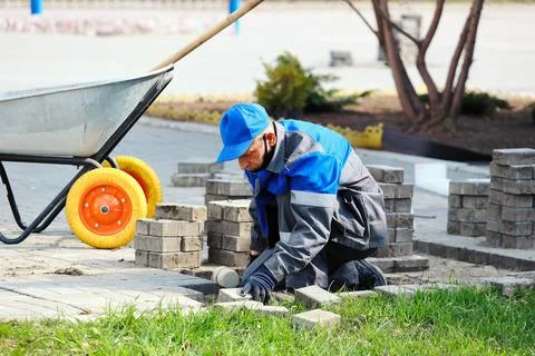 Bricklayer in work clothes sits on sidewalk and lays out paving slabs. Sight of Stock-Fotos