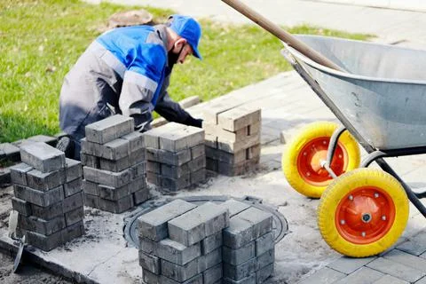 Bricklayer in work clothes sits on sidewalk and lays out paving slabs. Sight of Stock-Fotos