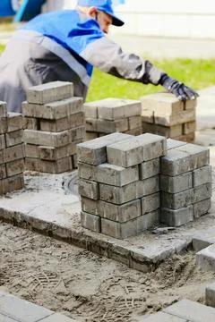Bricklayer in work clothes sits on sidewalk and lays out paving slabs. Sight of Stock Photos