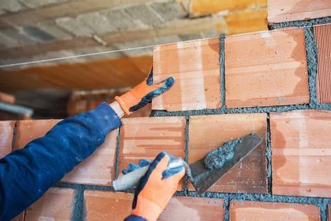 Bricklayer worker installing brick masonry on exterior wall with trowel putty Stock Photos