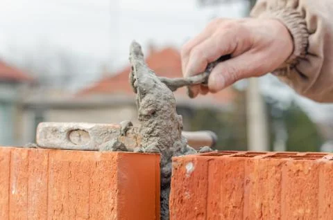 Bricklayer worker installing brick masonry on exterior wall with trowel putty Stock Photos