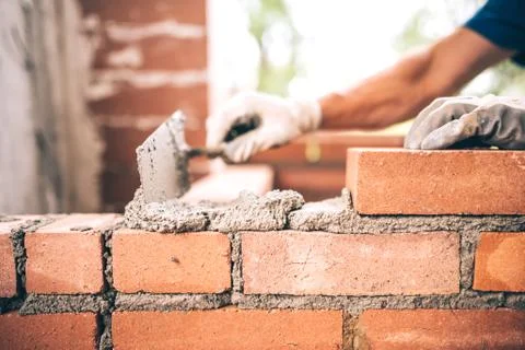 Bricklayer worker installing brick masonry on exterior wall with trowel putty Stock Photos