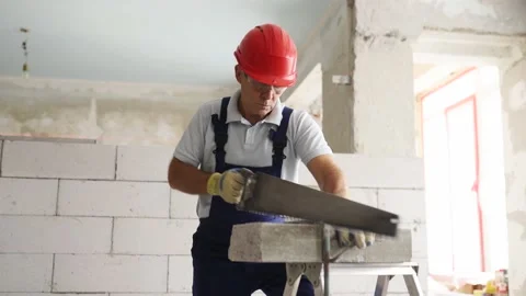 Bricklayer worker sawing foam concrete block with hand saw. Contractor cuts Stock Footage 199308255
