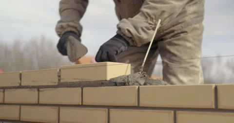 Bricklayer works at construction site, lays bricks in masonry, builds house Video stock 130780406
