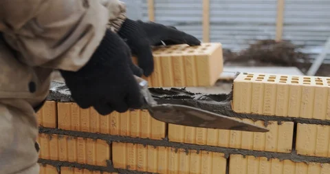 Bricklayer works at construction site, picks up brick, puts into prepared mortar Stock Footage 129838080