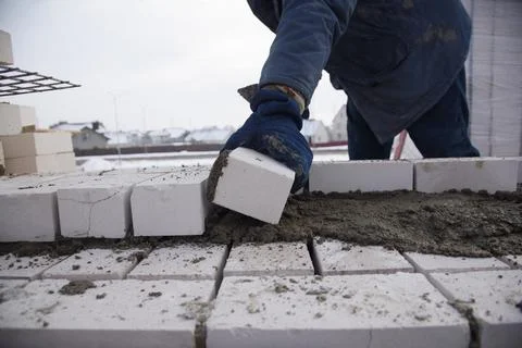 A bricklayer works on a construction site, putting bricks in the cement. 스톡 사진