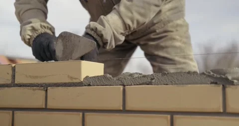 Bricklayer works at construction site, taps masonry with trowel, builds wall 動画素材 130368199