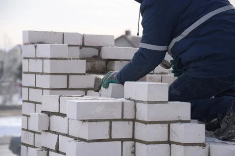 A bricklayer works on a construction site, a worker puts bricks in the cement. Stock Photos