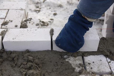 A bricklayer works on a construction site, a worker puts bricks in the cement. Stock Photos