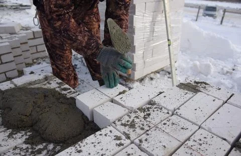 A bricklayer works on a construction site, a worker puts bricks in the cement. Stock Photos
