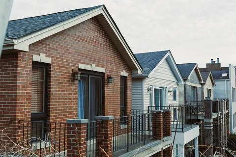 Bricks and siding form homes on a street under a cloudy sky in the afternoon Stock Photos