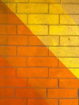 Bricks are painted in orange and yellow colors creating a pattern on a wall.  Stock Photos