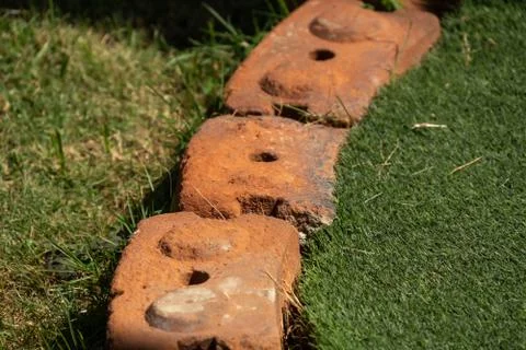 Bricks between artificial grass and the grass in the garden. Stock Photos