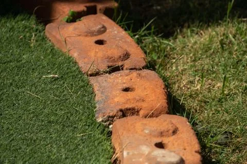 Bricks between artificial grass and the grass in the garden. Stock Photos