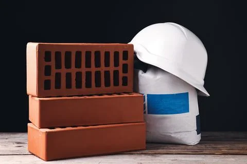 Bricks, hardhat and bag of cement on wooden table Stock Photos