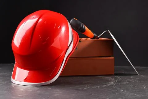Bricks, hardhat and bucket trowel on grey table Stock Photos