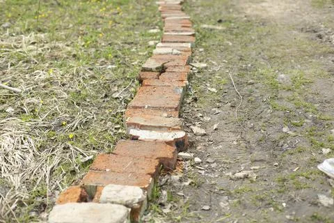 Bricks lie on road. Red brick encloses lawn. Stock Photos