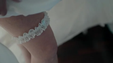 Bride adjusting a delicate white lace garter on her leg, captured in an Stock Footage 282727876