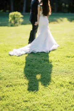 Bride and groom casting long shadow on green lawn Stock Photos