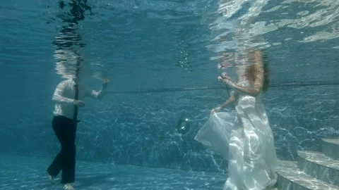 The bride and groom dive to the bottom of the pool in white wedding dresses on a 스톡 동영상 106715415
