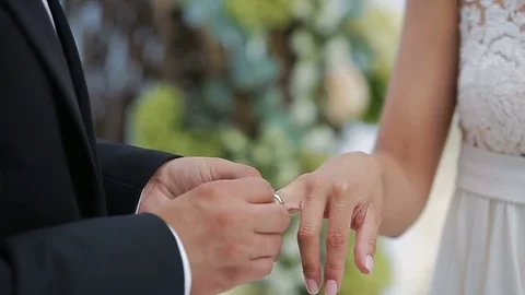 The bride and groom exchange wedding rings against a background of flower Stock Footage