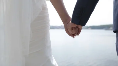 Bride and groom hold hands on a blue lake background. Stock Footage 79656631