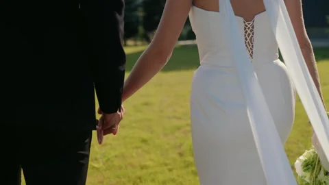 Bride and groom holding hands while walking on the grass Stock Footage 343909700