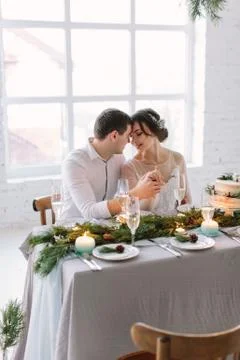 Bride and groom posing at the decorated banquet table in the white hall. Hand in Stock Photos