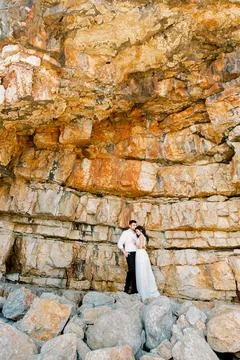 Bride and groom stand embracing on a sheer cliff Stock Photos