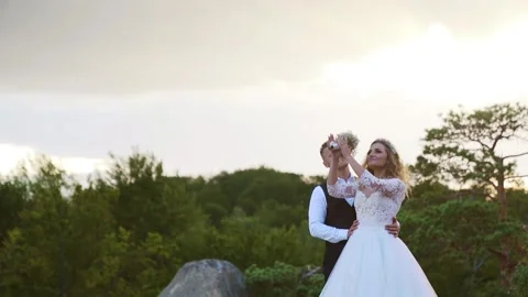 Bride and groom standing on a cliff at sunset, a blue clouds in background Stock Footage 234086576