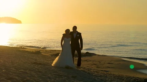 Bride and groom walking on the beach in the sunset Stock Footage 99490696
