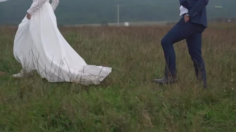 Bride and groom walking through large field of grass Stock Footage 157499090