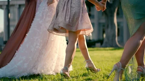 A bride and her three friends walk hand in hand on green grass. Video stock 233290993