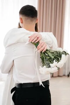Bride embracing groom while holding white bouquet behind his back Stock Photos