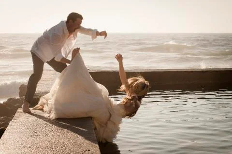 Bride falling into a pool of water with her husband trying to catch her. Stock Photos