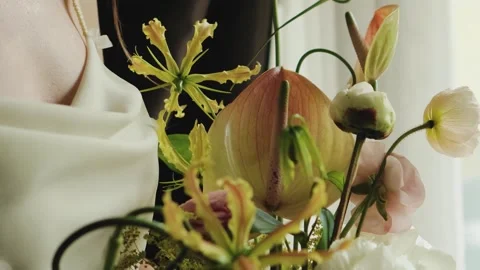 Bride holding wedding bouquet while standing by window in soft, warm, natural Video stock 323395214