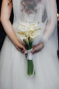 Bride holds elegant white calla lilies wrapped in pearls Foto stock