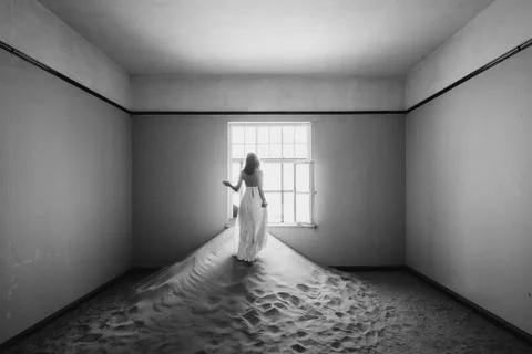Bride looking outside windows of an abandoned desert villa filled with sand Stock Photos